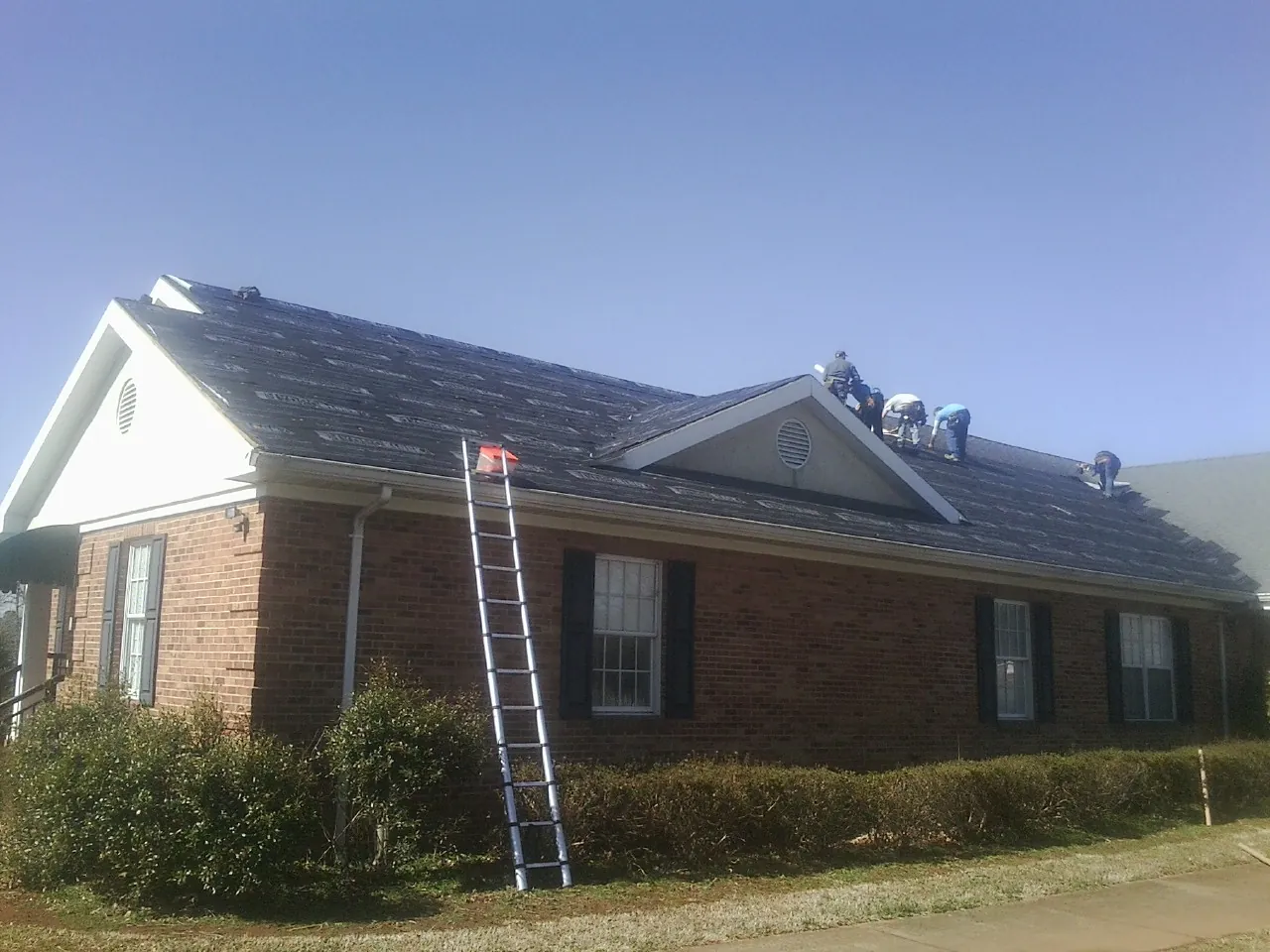 Crew tearing shingles off a brick ranch roof with a ladder set — Emergency Roof Repair work by our crew in Ash
