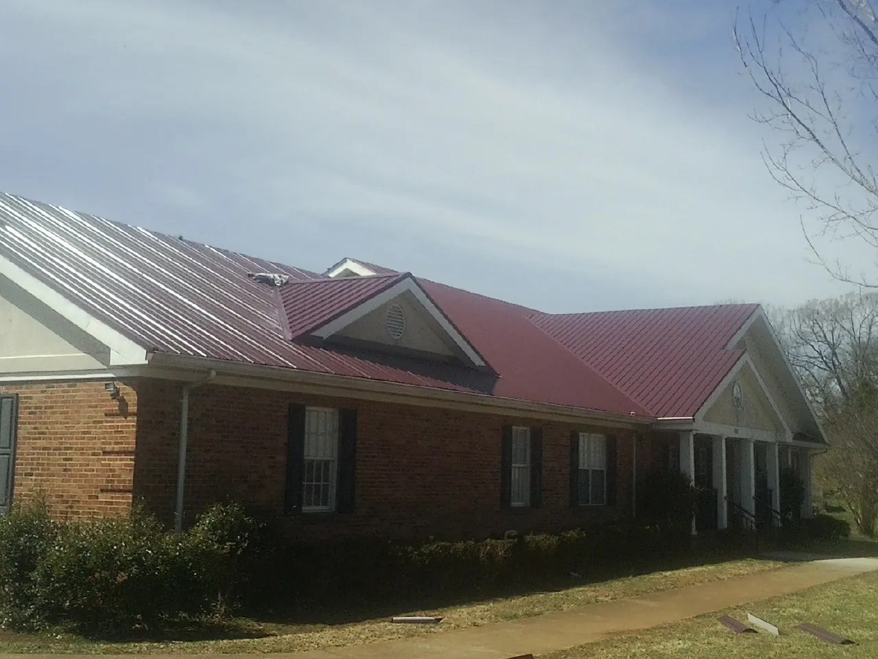 Red metal roof with gabled entries on a long brick building, from a Hail Damage Roof Repair job in Ash