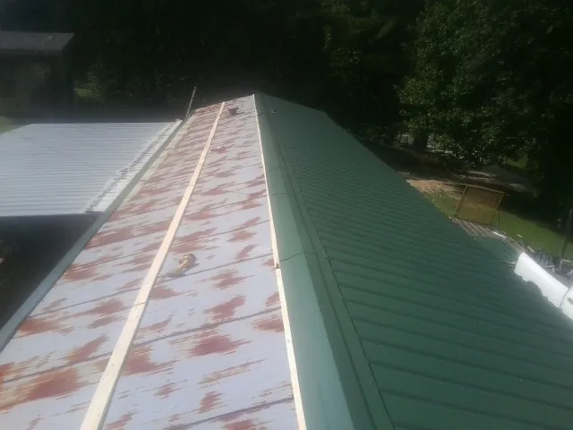 Old rusted panels beside newly installed green metal roofing — Wind Damage Roof Repair by Roofing Brothers in Ash