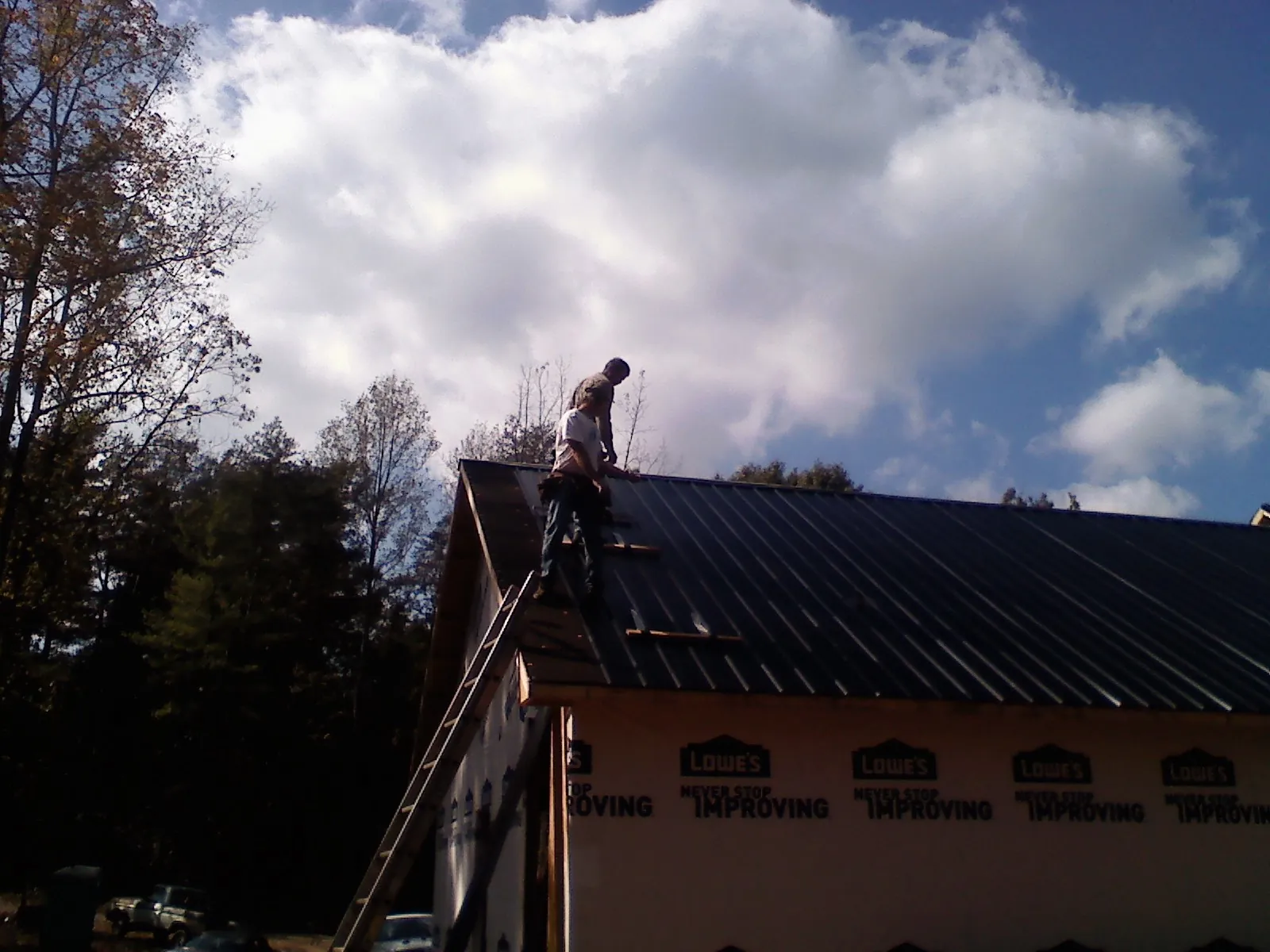 Roofer fastening dark metal panels high against a cloudy sky, from a Roof Inspection job in Ash