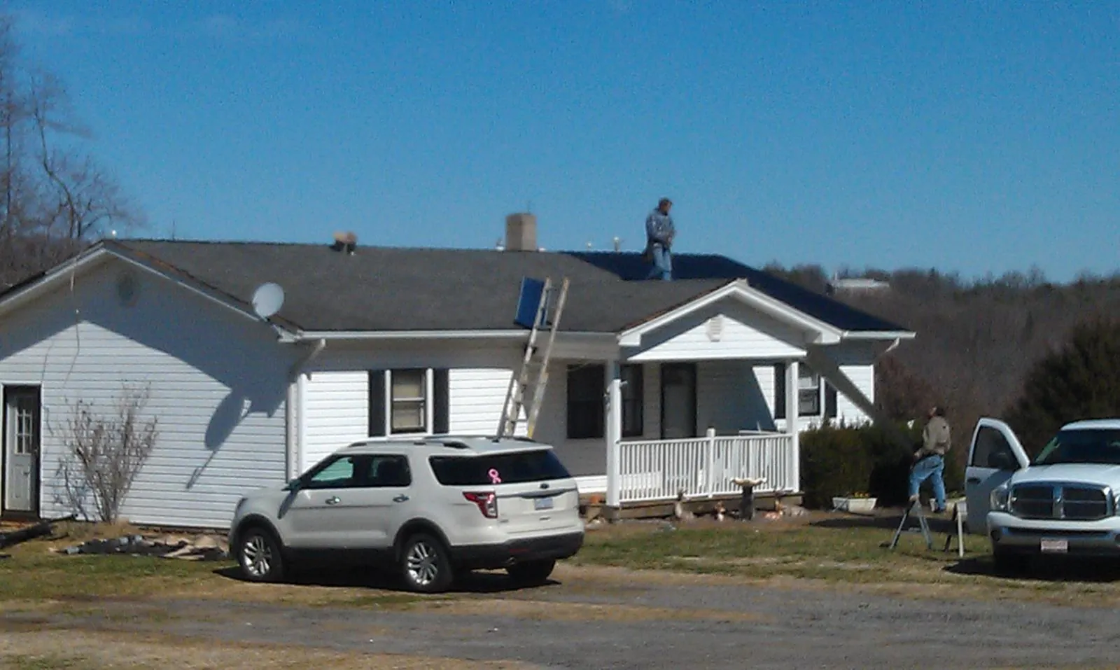 Roofers stripping shingles from a white ranch house roof in Ash
