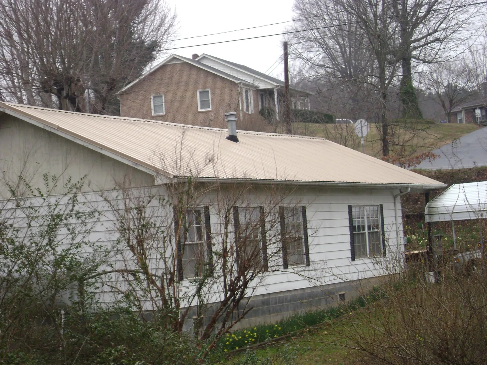 Tan metal roof on a white sided house set into a hillside — Commercial Roofing by Roofing Brothers in Ash
