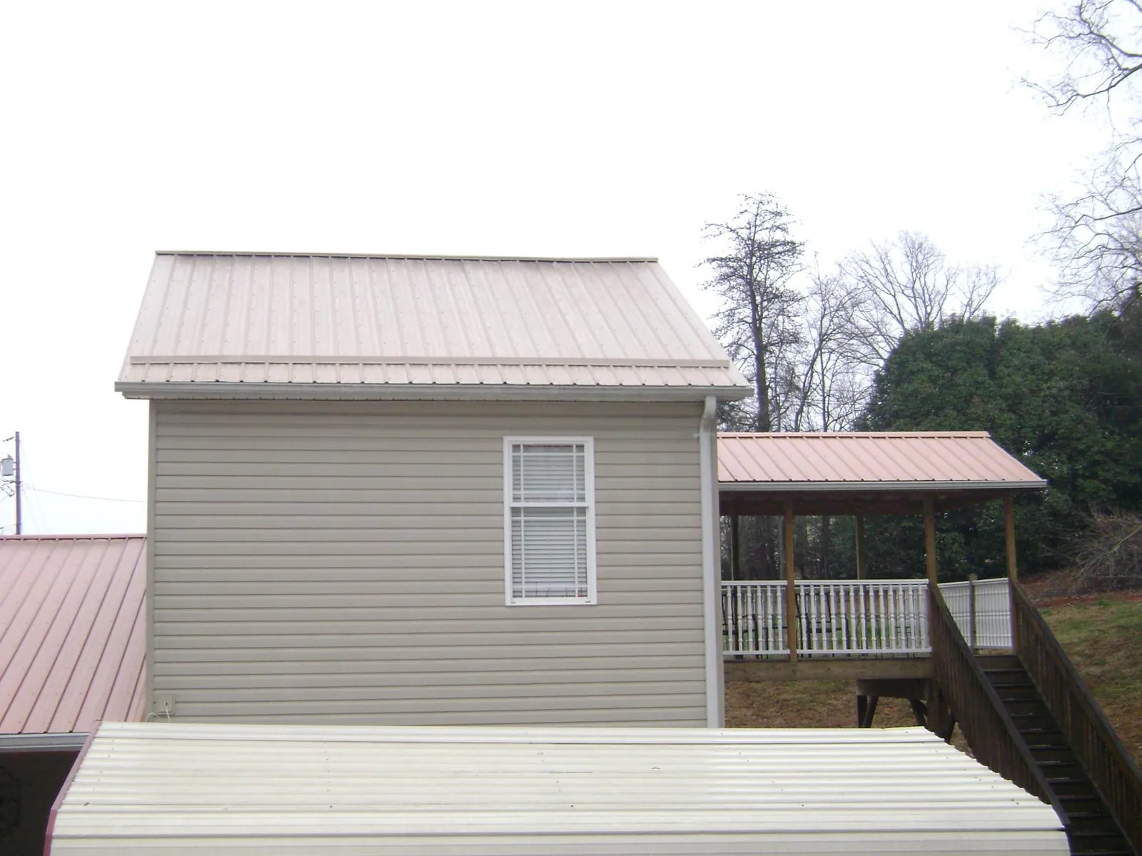 Tan metal roofs on a two story addition and attached porch, from a Roof Replacement job in Ash